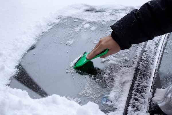 image of driver removing snow from windshield in winter